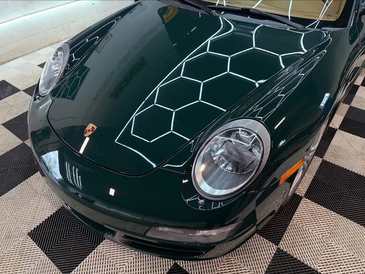 Close-up of the gloss emerald green PPF on a Porsche 911 hood reflecting the hex lights