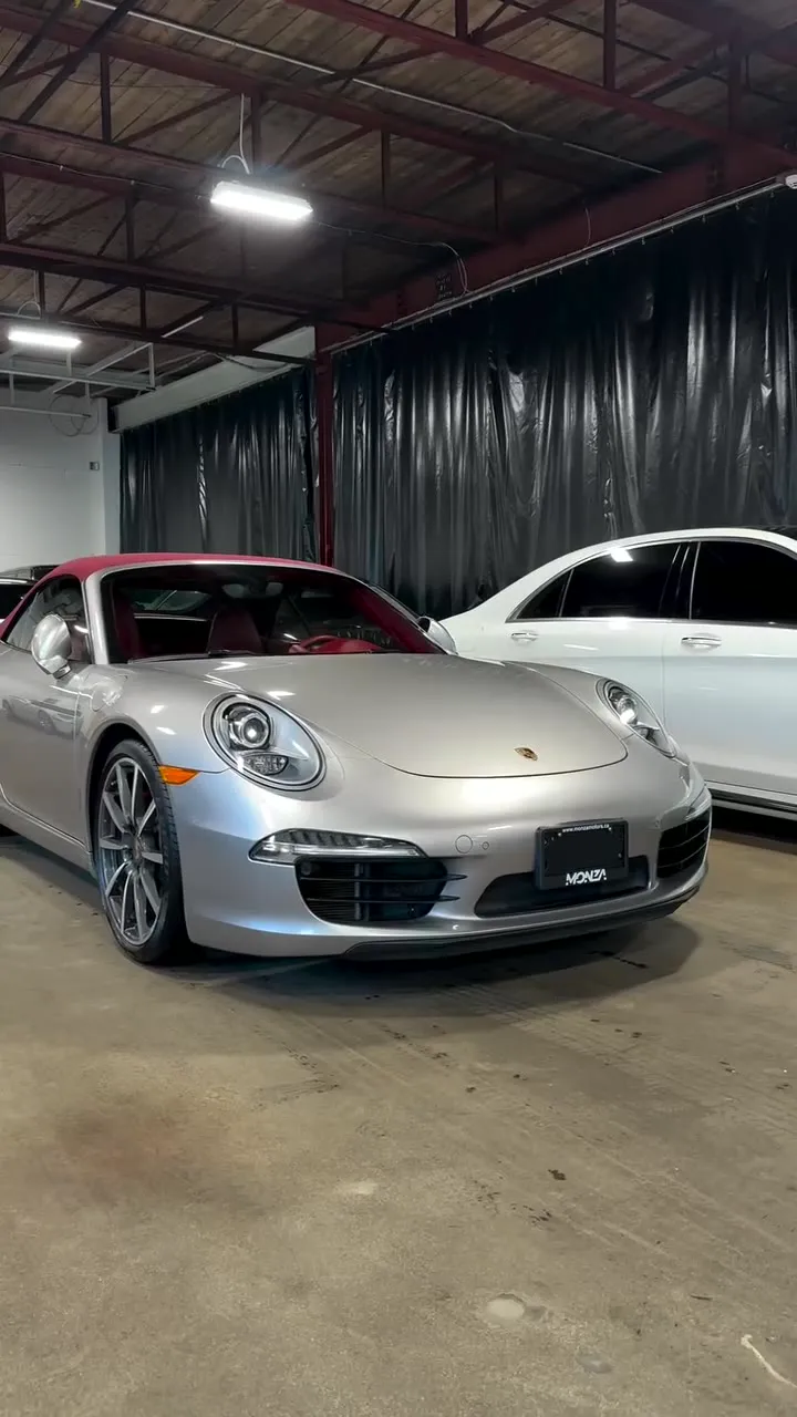 A silver Porsche 911 and a white car lined up inside the AVG bay